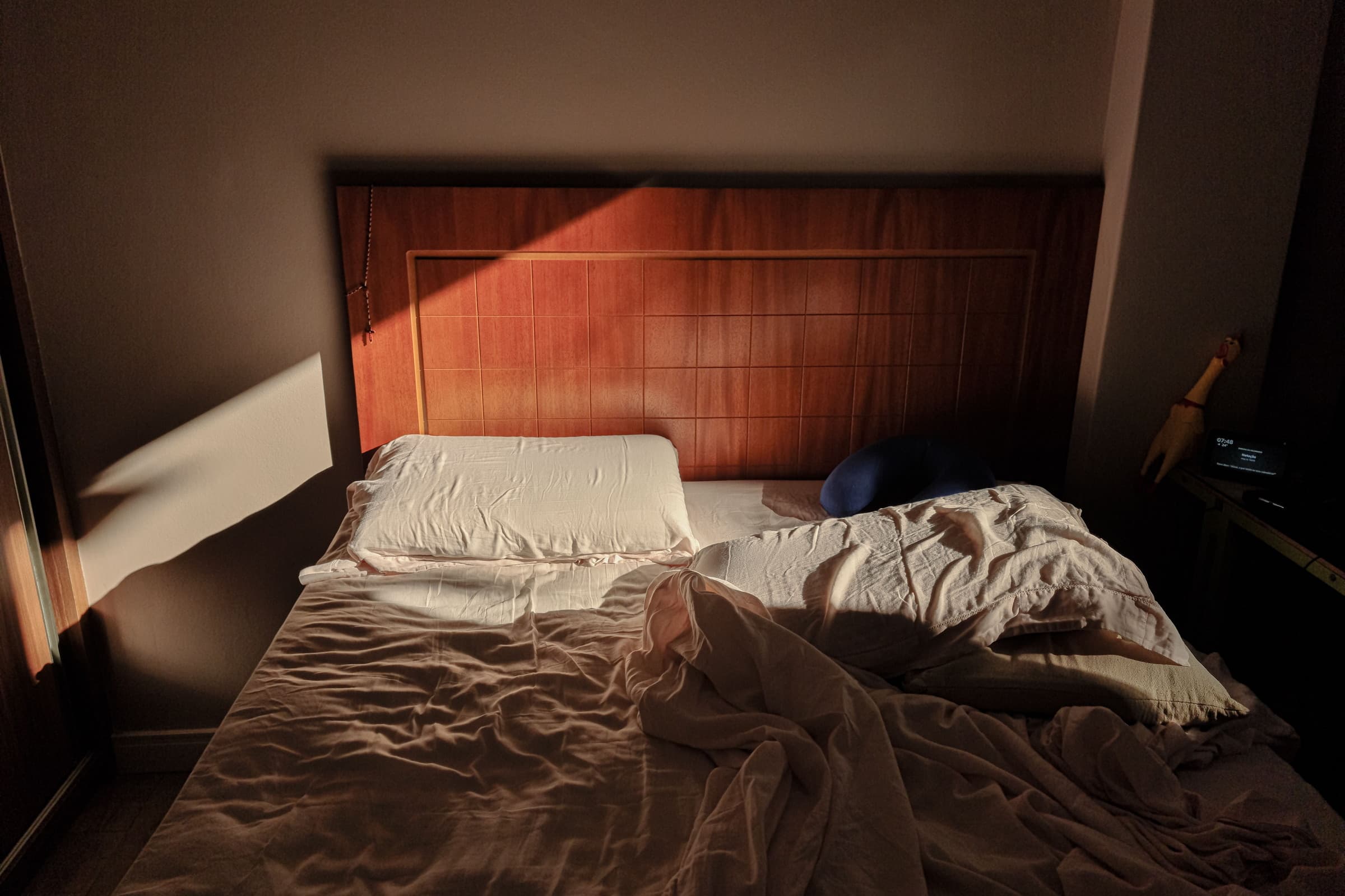 A bed with the covers thrown back, a wide band of low sun falling across it from a window out of frame.