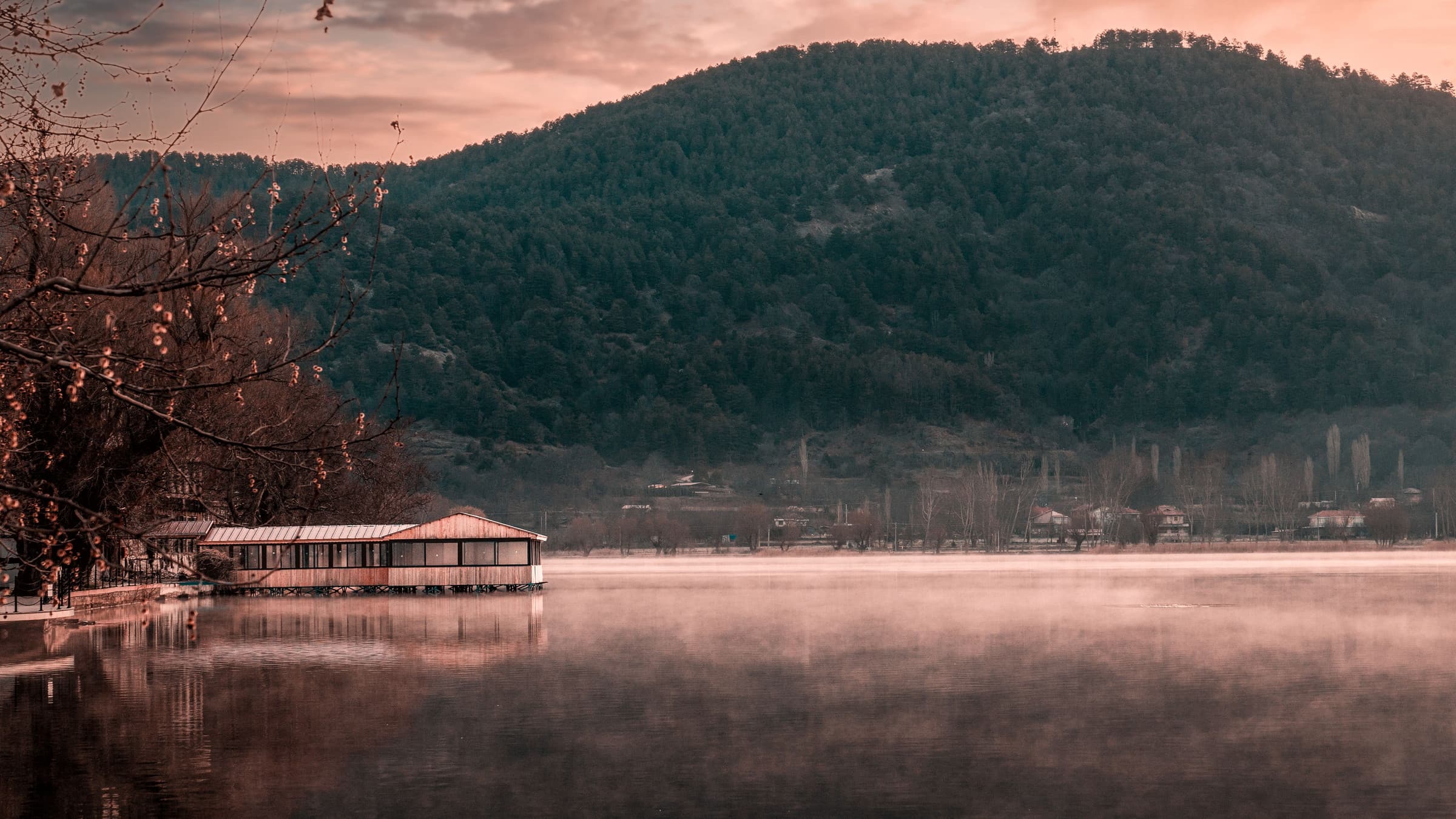 Mist lying on a still lake at sunrise, a timber pier reaching out from the shore and wooded hills rising behind.